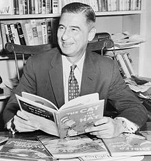 Theodor Seuss Geisel surrounded by his literary works. He holds one of his most popular, The Cat in the Hat.